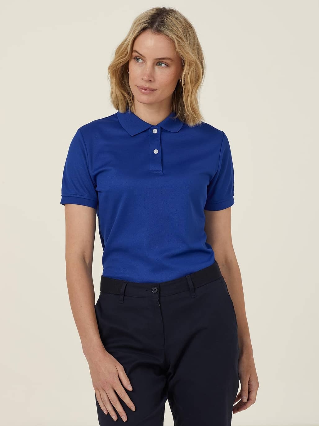 Woman wearing a blue polo shirt and black pants on a beige background