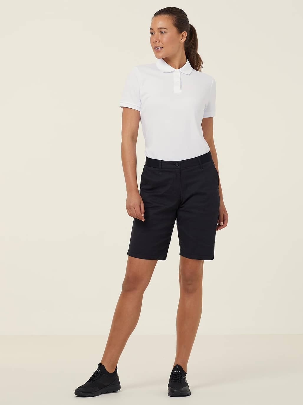 Woman wearing a white polo shirt and black shorts on a beige background