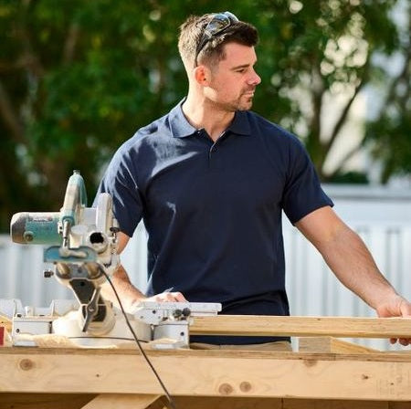Man working with a power tool on a wooden surface outdoors