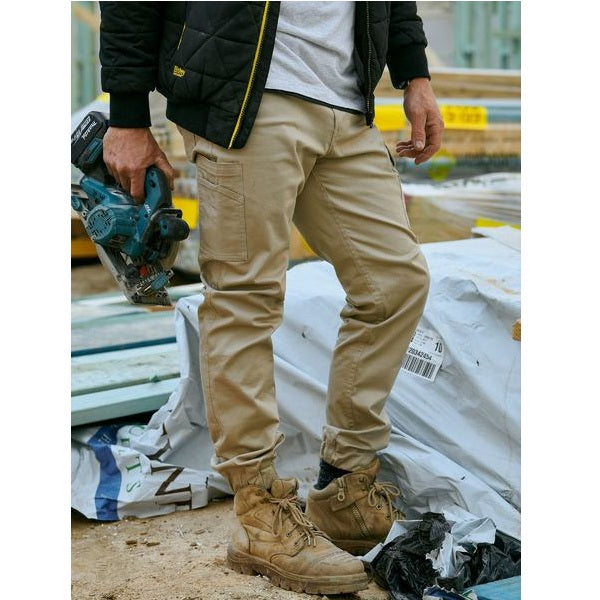 Person wearing beige work pants and brown boots holding a power tool on a construction site.