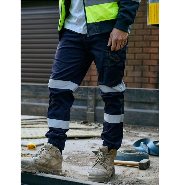 Person wearing navy work pants with reflective stripes and a high-visibility jacket in an industrial setting.
