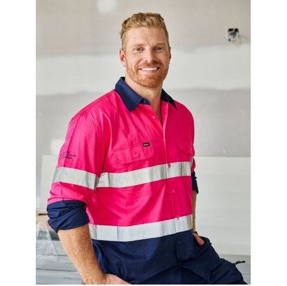Man wearing a bright pink and navy work shirt with reflective stripes indoors.