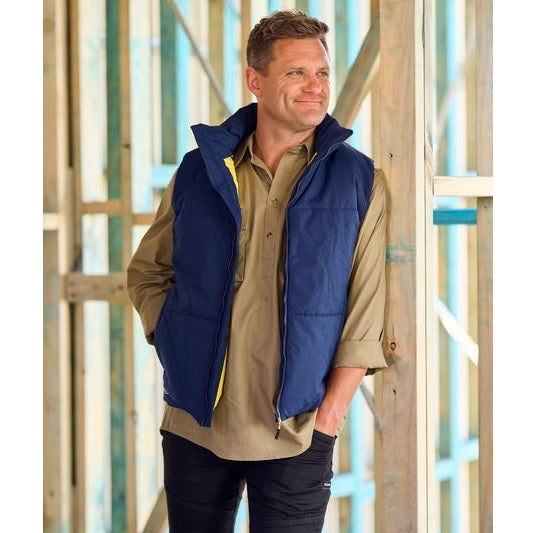 Man wearing a blue vest over a beige shirt in a construction setting