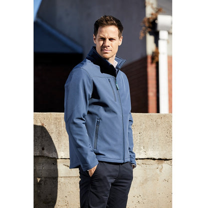 Man wearing a blue jacket standing against a concrete wall.