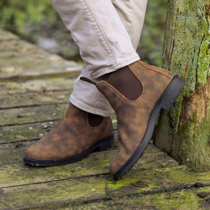 Brown leather shoes worn with light-colored pants on a wooden surface with a natural background K92075