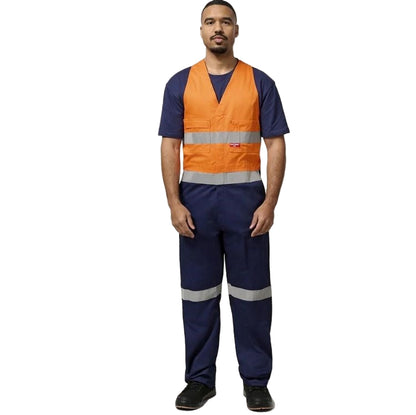 Person wearing an orange safety vest and navy work pants with reflective stripes on a plain background