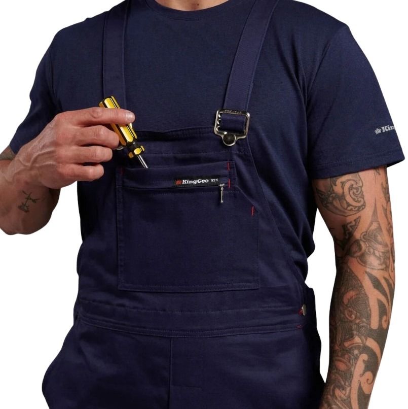 Person wearing navy blue work overalls holding a tool, with tattoos visible on arms.