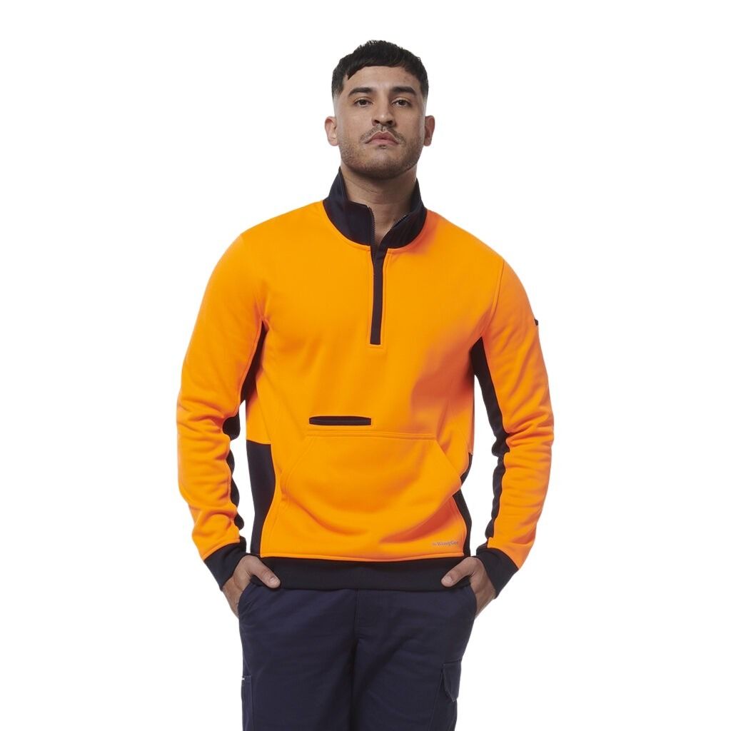Man wearing an orange and black pullover with navy pants on a white background