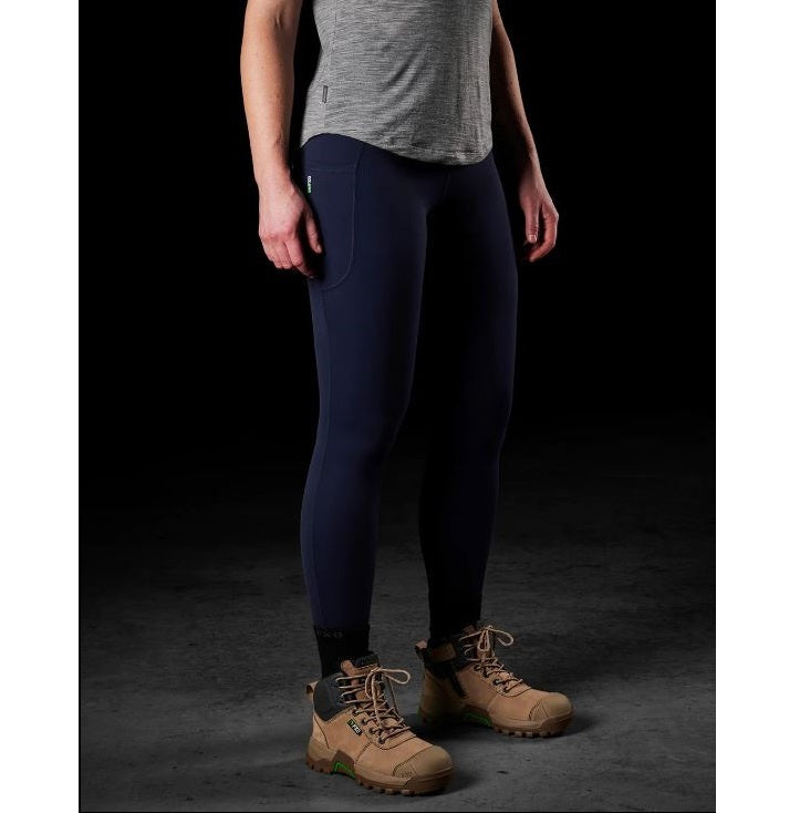 Person wearing navy leggings and brown boots on a dark background