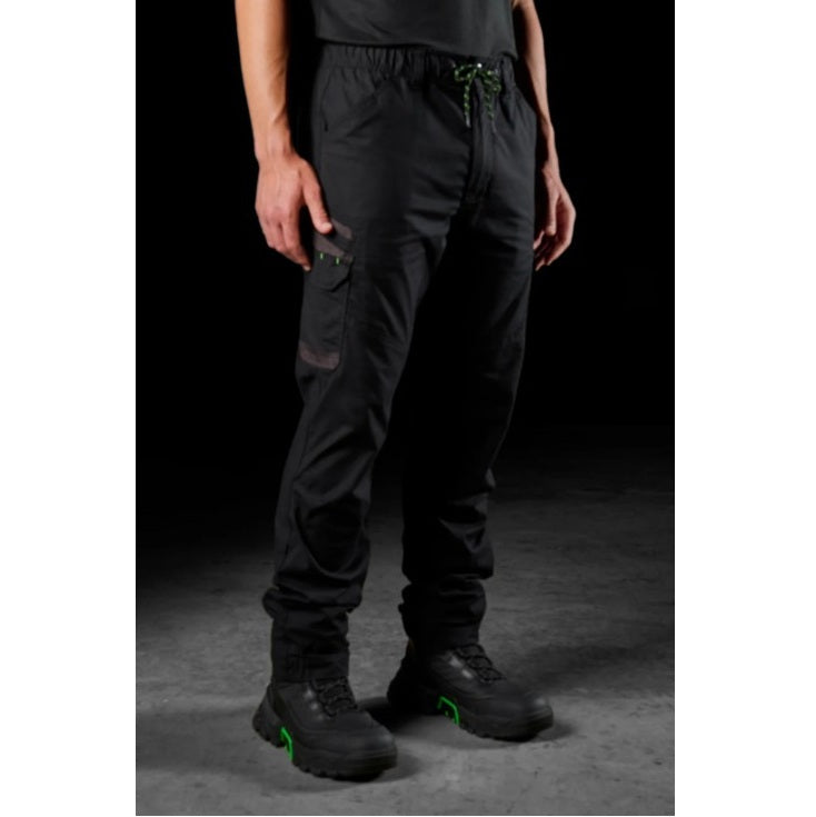 Person wearing black tactical pants and boots with green accents on a dark background